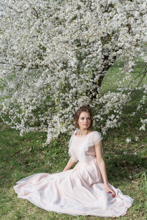 beautiful tender sweet girl in a pink dress with a hairdo near blossoming tree on a sunny spring dayの写真素材