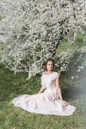 beautiful tender sweet girl in a pink dress with a hairdo near blossoming tree on a sunny spring dayの写真素材