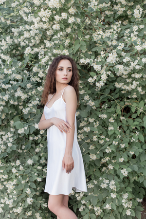 beautiful cute tender girl with dark hair in a white summer dress with a jasmine flower in handsの写真素材