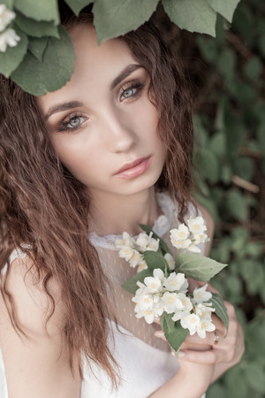 beautiful cute tender girl with dark hair in a white summer dress with a jasmine flower in handsの写真素材