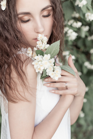 beautiful cute tender girl with dark hair in a white summer dress with a jasmine flower in handsの写真素材