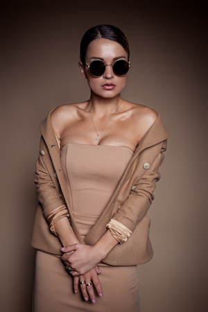 beautiful business woman in a business dress and glasses on a brown background in the studioの写真素材