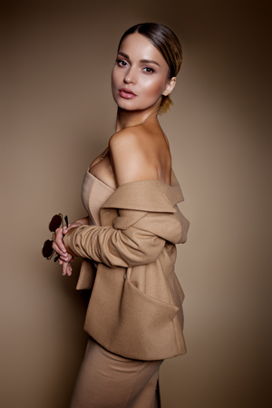 beautiful business woman in a business dress and glasses on a brown background in the studioの写真素材