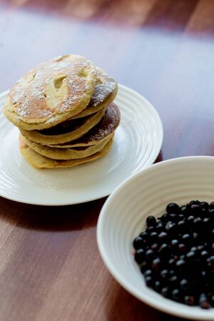 pancakes with berries and powdered sugar in a white plate are on the tableの写真素材