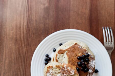 pancakes with berries and powdered sugar in a white plate are on the tableの写真素材