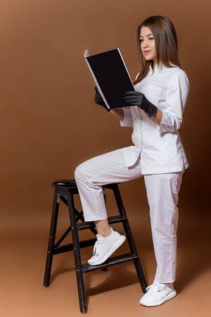 girl medical worker in black gloves in a white suit with a magazine in her handsの写真素材