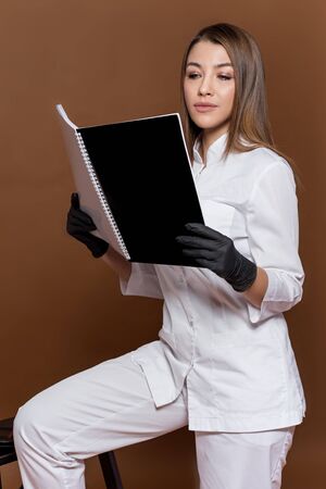 girl medical worker in black gloves in a white suit with a magazine in her handsの写真素材