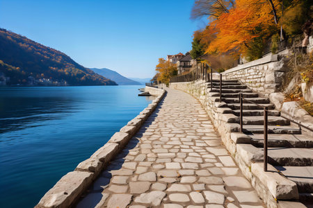 Serene Lakeside Path with Cobblestone Walkway and Autumn Trees Reflecting in Calm Waterの素材