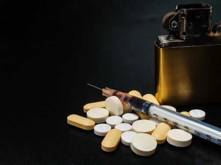 A pills and injection syringe with cocaine and golden vintage Cigarettes lighter on darkness backgroundの写真素材