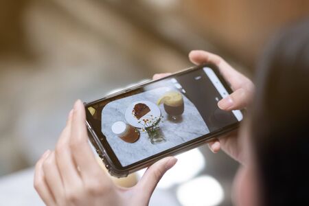 A girl take a picture of coffee and cake by smartphone in cafeの写真素材