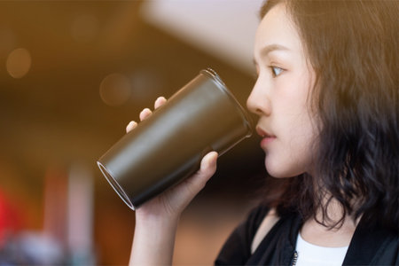 A woman drinking coffee by reuse black coffee bottle in coffee cafe
