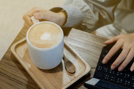 A girl drinking hot milk tea and typing something in cafe の写真素材
