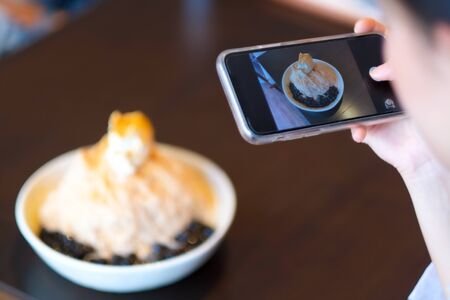 A girl take ice cream picture by smartphone camera in cafe の写真素材