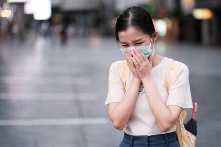 Asian girl sneezing in public areas with surgical mask,COVID-19,new normal lifestyleの写真素材