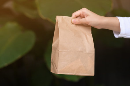 Woman holding paper bag with food outdoors, closeup. Space for textの写真素材