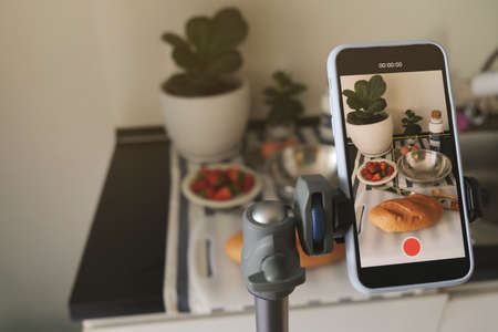 A young woman taking a video with her smartphone while making breakfast.の写真素材
