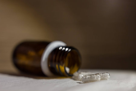 Pills coming out of a little glass bottle on a white surface.の写真素材