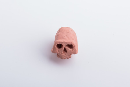 A part of an ugly skull made from orange clay, with it's jaw missing, on a white surface.の写真素材