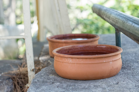 Two brown bowls made out of clay, put on a grey concrete base, full of water, for animals to drink, in a garden, during the hot summerの写真素材