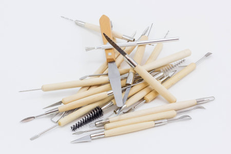 A pile of sculpture tools, made of wood and metal, on a white surface.