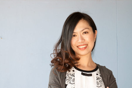 Beautiful Asian young businesswoman standing with hands folded against white background