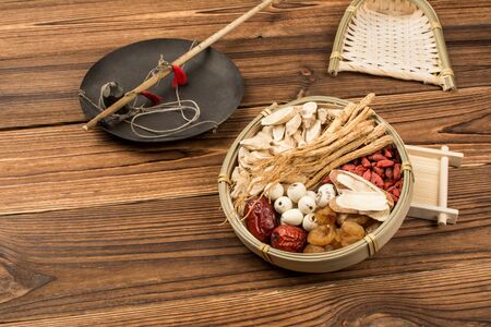 On the background of the wood grain, there is a rod and a plate of Chinese medicine. The plate contains ginseng, astragalus, licorice, medlar, red dates, longan and lotus seeds.の写真素材