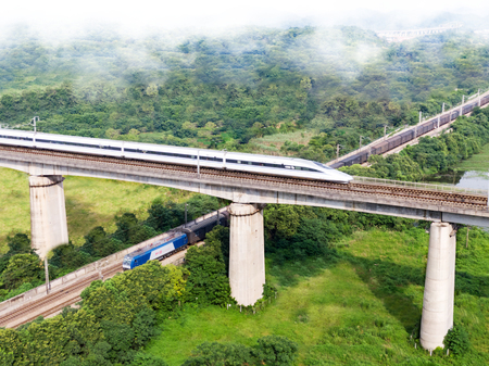On a green meadow, a traditional electric train passes underneath a high-speed rail locomotive on a viaductのeditorial素材