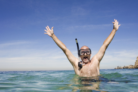 A mature man jumping in excitement with snorkeling gear on.の写真素材