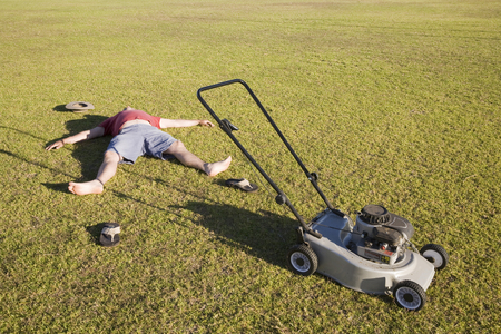 An exhausted man lying on the ground collapsed after mowing a huge lawn.の写真素材