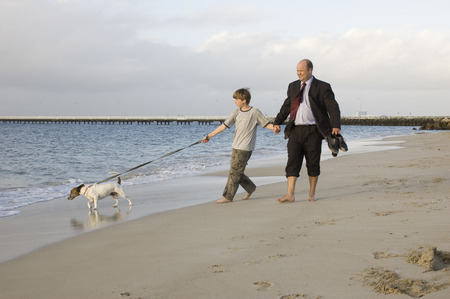 A father and son taking time out to walk the dog on the beach.の写真素材