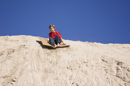 A boy using cardboard to slide down a sand dune.の写真素材