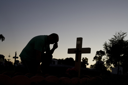 A man grieving or praying by a cross.の写真素材