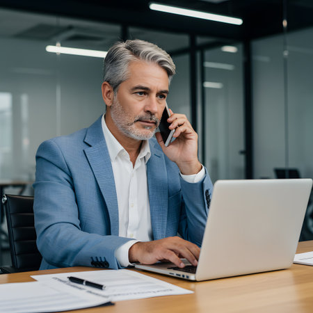 Experienced businessman on phone with laptop at deskの素材