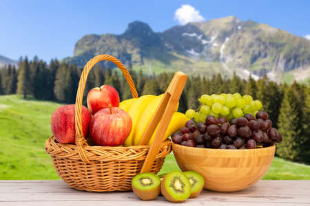 Group Healthy fresh fruit in a wooden basket, With vitamins c from bananas, kiwi, grapes, raspberries, blueberries, and blackberries, good for the body and diet food on the table in nature background.の写真素材