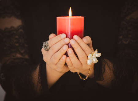 A picture of a woman holding a candle to perform magic rituals and mysteries about superstition in the concept of Divine magic & occultism on the old wooden table.の写真素材