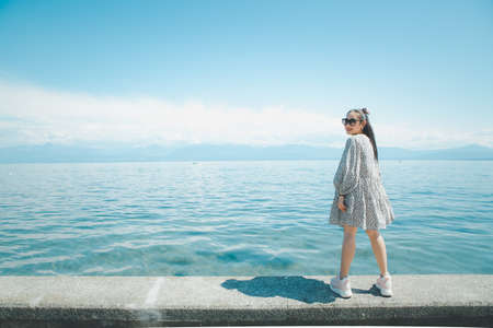 Beautiful Asian woman with white skin and long black hair Wearing black glasses. feeling happy to Sit on stone and watching the lake view On a clear sky day, Tourism and summer vacations.の写真素材