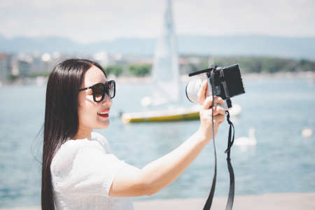 Asian beautiful woman is travel for holiday in the summer of Europe and taking a camera view landscape of lake and bright sky in Geneva Switzerland, copy space.の写真素材