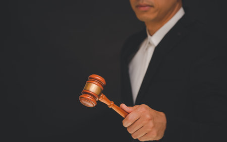 Businessmen are holding an old judge's hammer to use for judgment and justice in a black background.