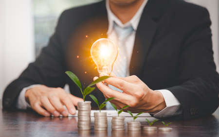 Businessman hand holding light bulb on coins stack on the wooden table , Saving ideas and investment budget, Creative ideas concept of saving money  concept, Copy spaceの写真素材