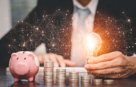 Businessman hand holding light bulb with line connect and Coins stack on the wooden table , Saving ideas and investment budget, Creative ideas concept of saving money  concept, Copy spaceの写真素材