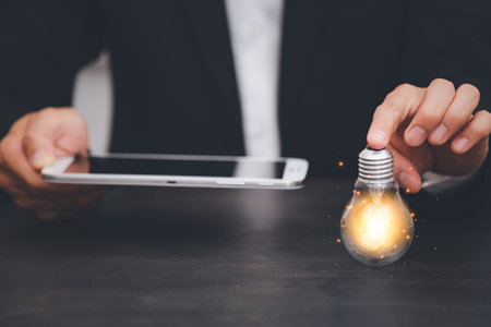Businessman holds the tablet and light bulb in graph Screen Icon of a media screen, Technology...