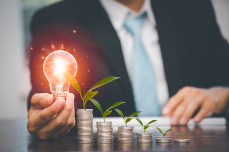 Businessman hand holding light bulb on coins stack on the wooden table , Saving ideas and investment...