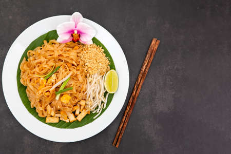 Pad thai is Thai food Noodle and tofu mixed with tamarind sauce and bean sprouts and spring onion in white dish put on the banana leaf in black backgroundの写真素材