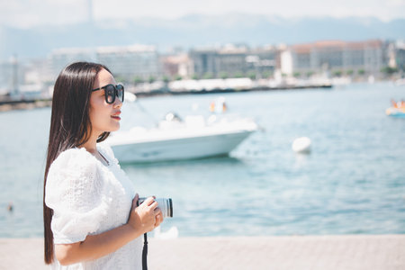 Asian beautiful woman is travel for holiday in the summer of Europe and taking a camera view landscape of lake and bright sky in Geneva Switzerland, copy space.の写真素材
