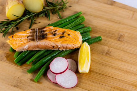 Grilled fresh salmon steak with roasted green beans, baked potatoes, lime and salad vegetables is a...