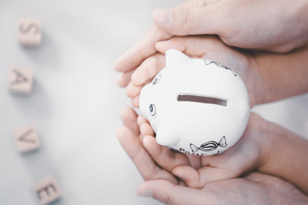White Piggy bank in  Hand family and wood word save money in the future for family background, Saving ideas  and investment budget, Business saving money concept, Copy spaceの写真素材