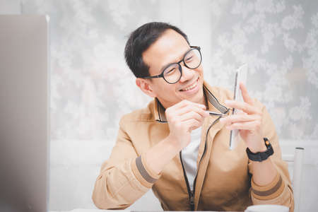 Asian man in casual clothing using a laptop communicates on the internet with the customer at  kitchen table at home. concept work from home.の写真素材