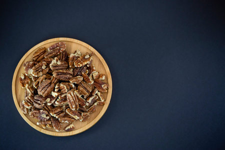 pecan nut or Pekannuss nuts group Protein and healthy food for diet in a wooden plate on a black...