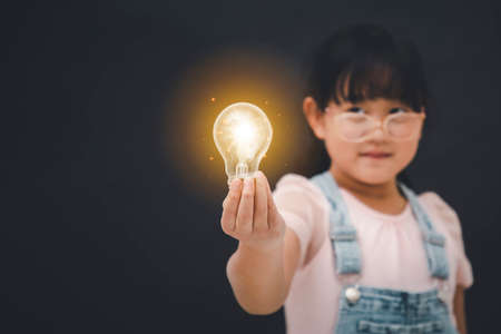 Asian Little girl holding light bulb in the black background, ideas with innovative technology and Electricity, education and people conceptの写真素材
