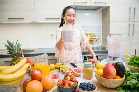 Happy woman enjoy preparing freshly squeezed fruits with vegetables for making smoothies for breakfast together in the kitchen.diet and Health concept.の写真素材